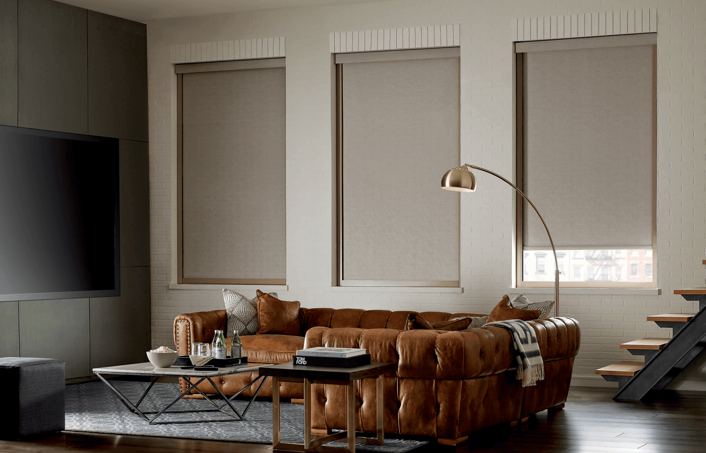 Neutral roller shades above a brown leather living room sofa